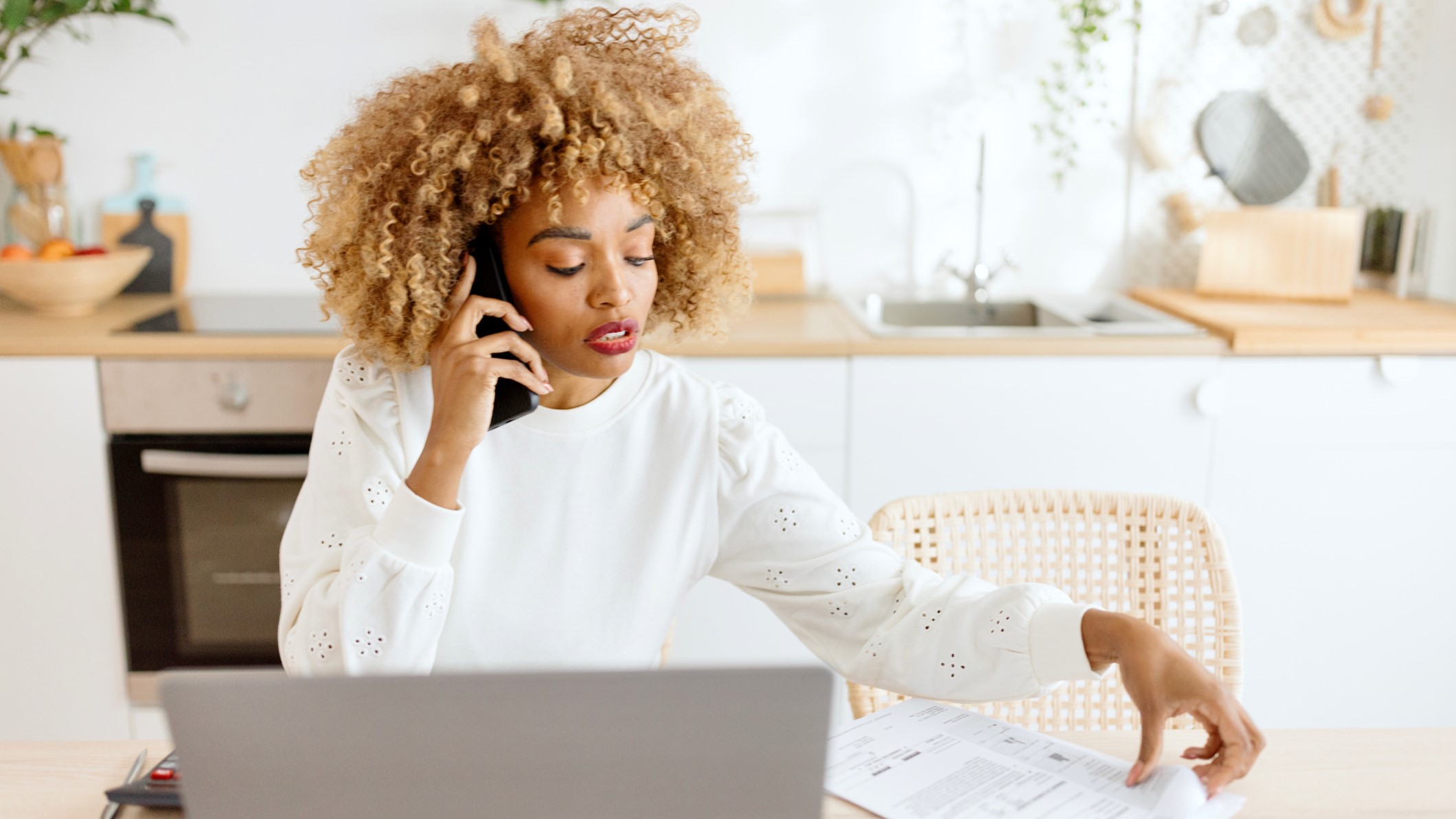 women talking on phone looking over phonebill with laptop before her