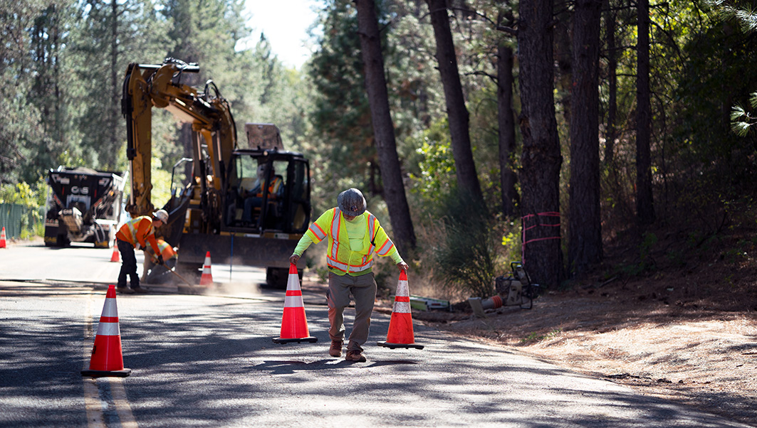 A worker picking up traffic cones while construction work happens behind him.