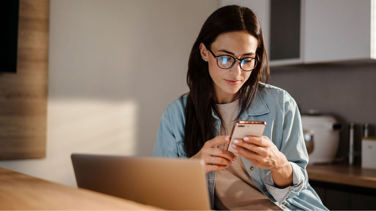 Woman looking at her phone with an laptop in front of her