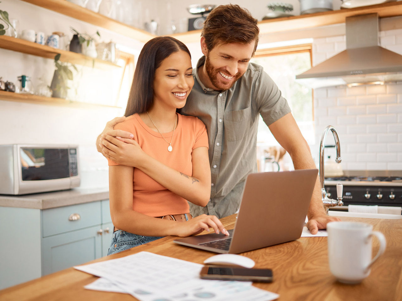 Two people stand in a kitchen looking at a laptop