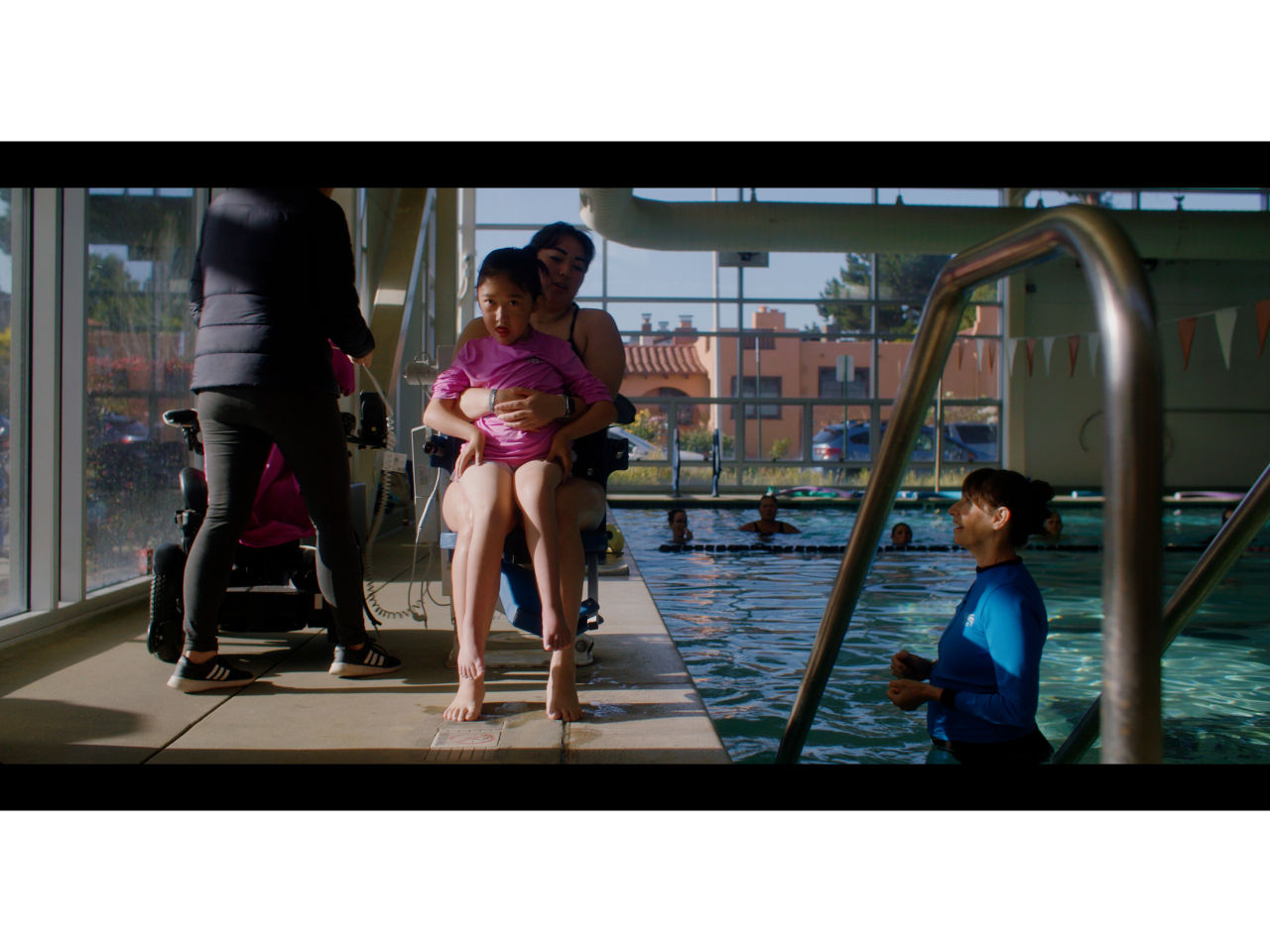 Un voluntario de SNAPkids ayuda a Olivia a entrar en la piscina