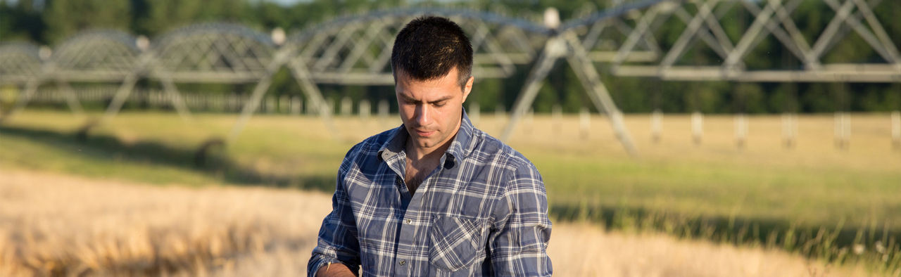 man standing in field looking at water pumps