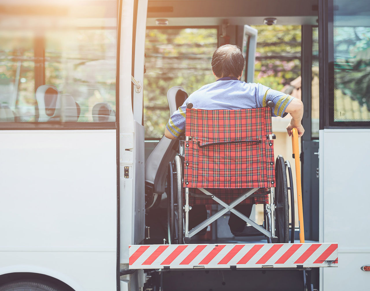 A person in a plaid wheelchair is being lifted into a white bus using an accessibility ramp or lift.