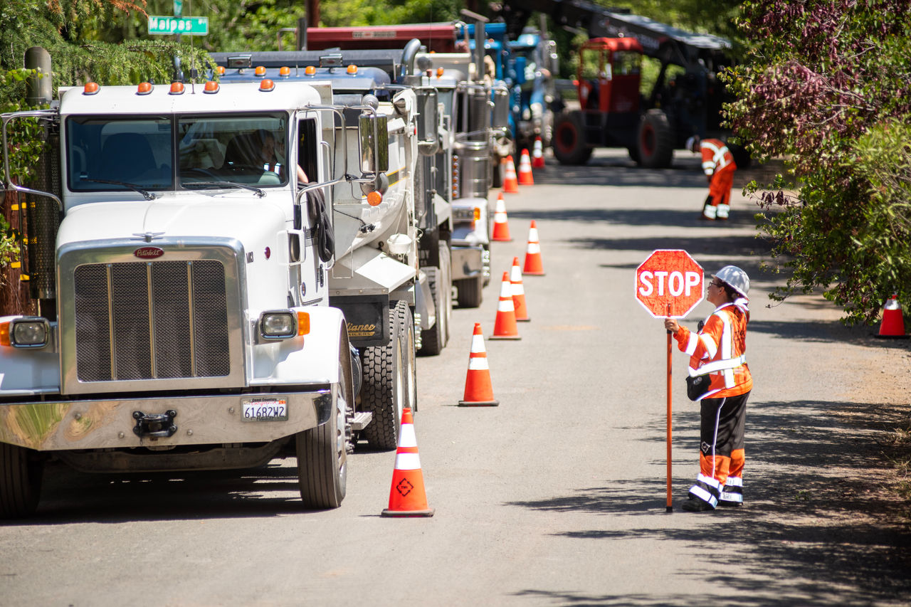  Crew member holding a “STOP” sign with construction vehicles behind a line of traffic cones