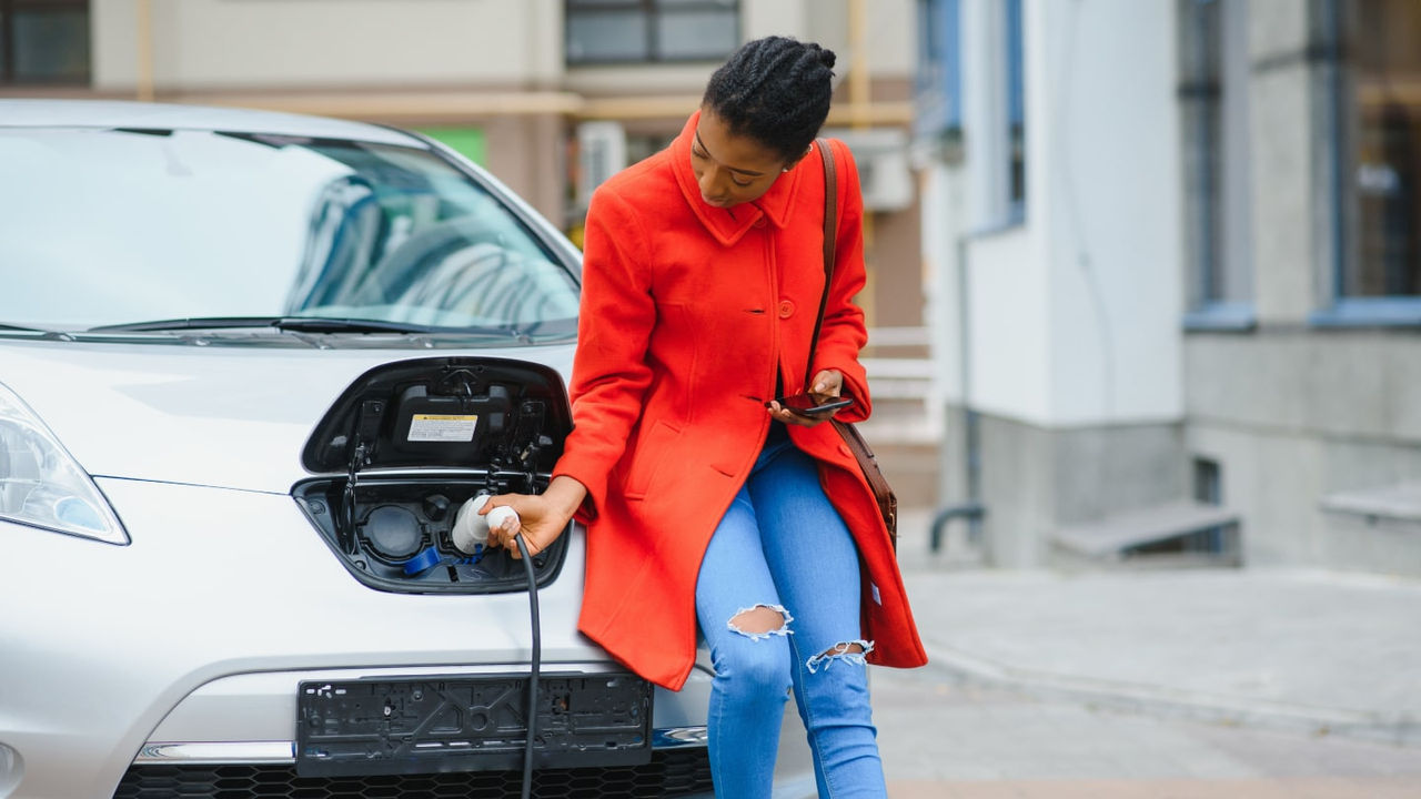 A person in a red coat charging their electric motor vehicle.
