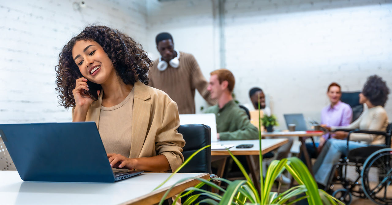 Mulher a olhar para um computador portátil e ao telefone num espaço de trabalho