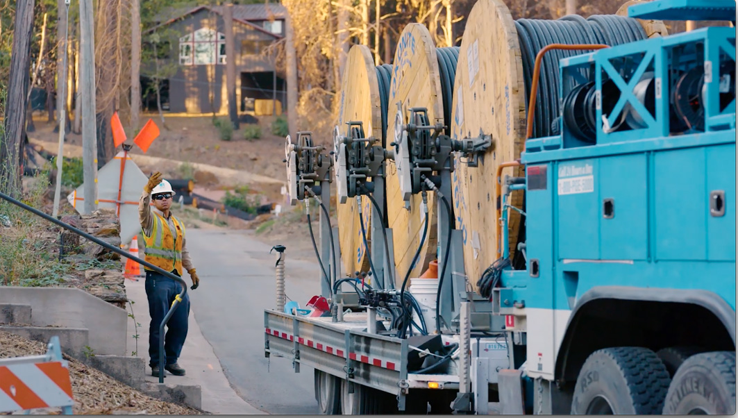PG&E truck carrying cable with crew member flagging it down.